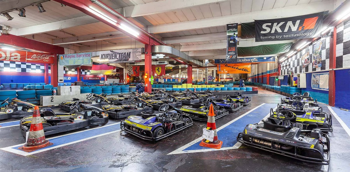 Die Kartbahnhalle mit vielen, aufgestellten Go-Karts im Vordergrund und der Strecke im Hintergrund