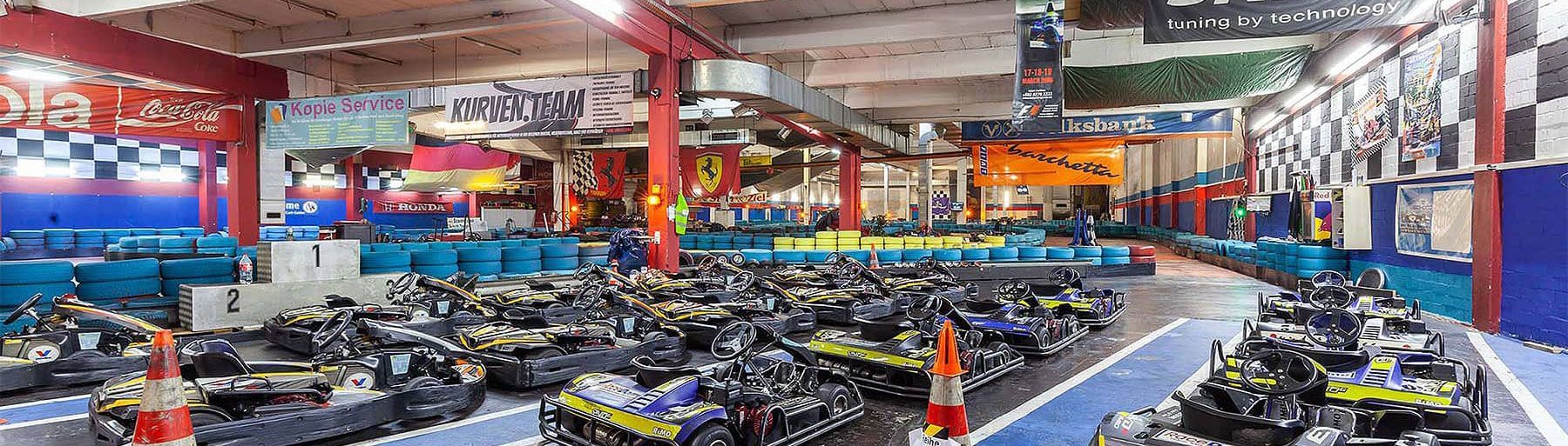 Die Kartbahnhalle mit vielen, aufgestellten Go-Karts im Vordergrund und der Strecke im Hintergrund